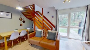 Una sala de estar moderna con una escalera de madera, un comedor con mesa y sillas, y un gran ventanal corredero que da a un jardín.