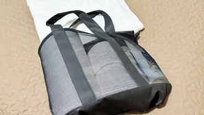 Eine schwarze und graue Netztasche mit einem weißen Stoff darüber, auf einer strukturierten beigen Oberfläche platziert.