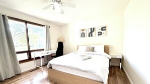 Ein Schlafzimmer mit einem Bett, einem Schreibtisch, einem Stuhl, einem Deckenventilator und Bildern an der Wand.