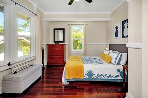 Ein Schlafzimmer mit einem Bett, einer Bank, einem Schminktisch, einem Fenster und einem Deckenventilator.