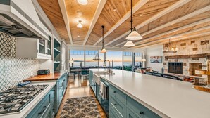 A modern kitchen with a large island, wooden ceiling beams, and a view of the ocean.