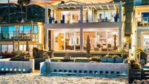A modern two-story house with a balcony, outdoor seating, and a pool area.