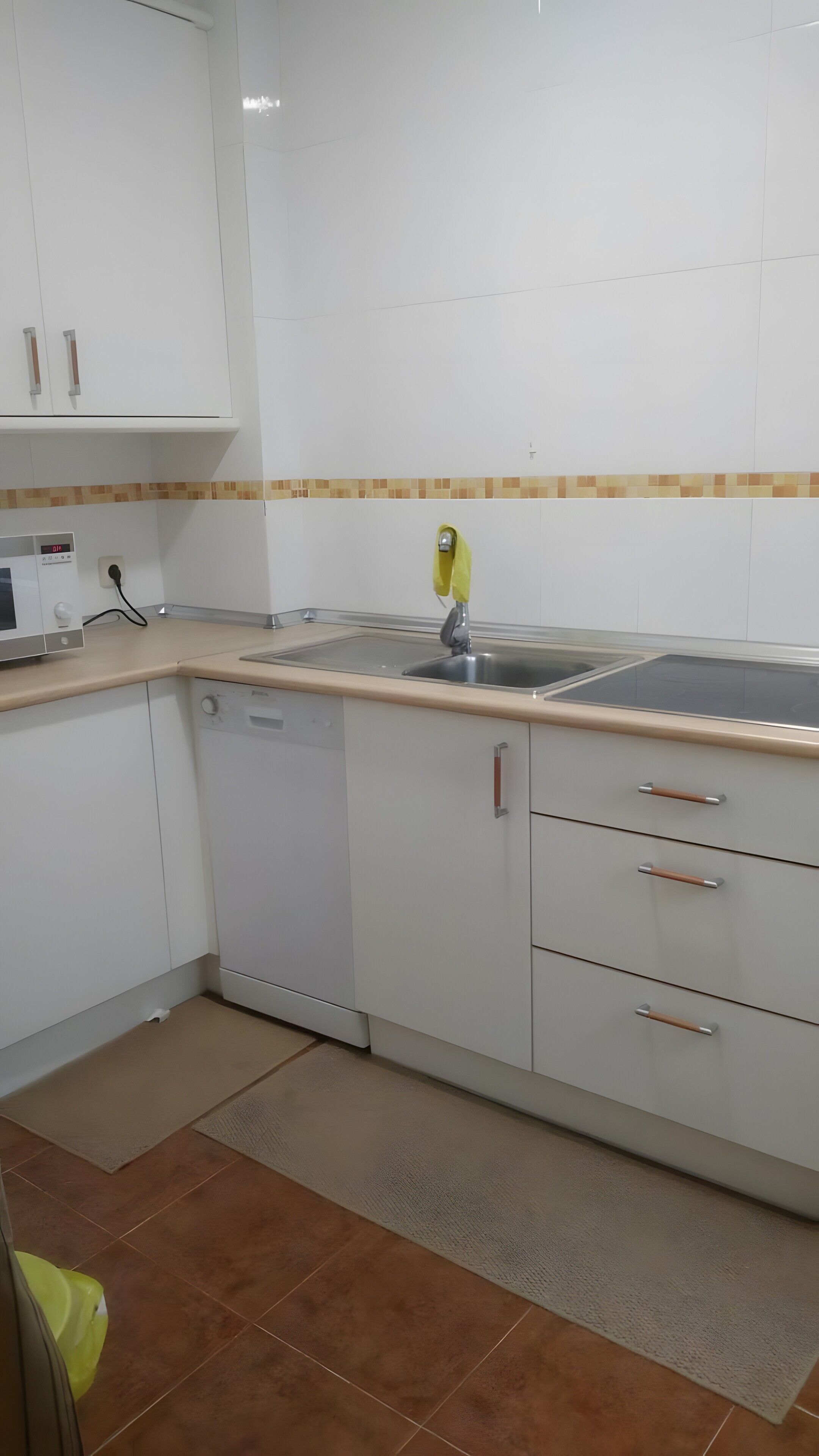 Una cocina con armarios blancos, un lavamanos de acero inoxidable y un microondas.