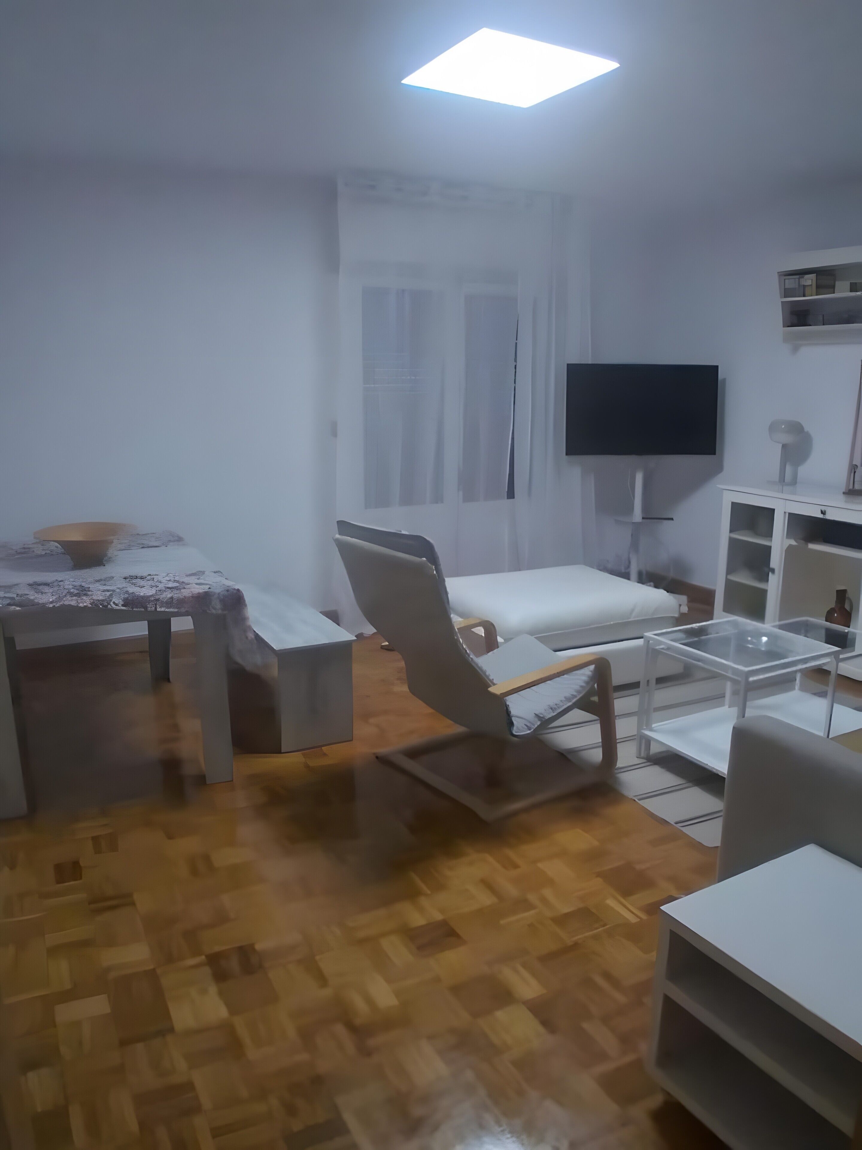 Uma sala de estar com sofá, mesa de centro, televisão e janela com cortinas.