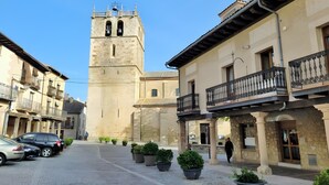 Une place historique pavée de pierres, dominée par une tour imposante et bordée de bâtiments traditionnels dotés de balcons.
