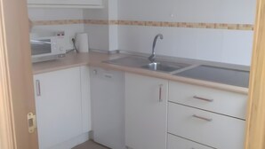 Une cuisine avec des meubles blancs, un four à micro-ondes, un évier et un pare-feu en carrelage.