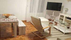 Une pièce comprenant une table à manger en bois, un canapé blanc, un téléviseur et un meuble blanc.