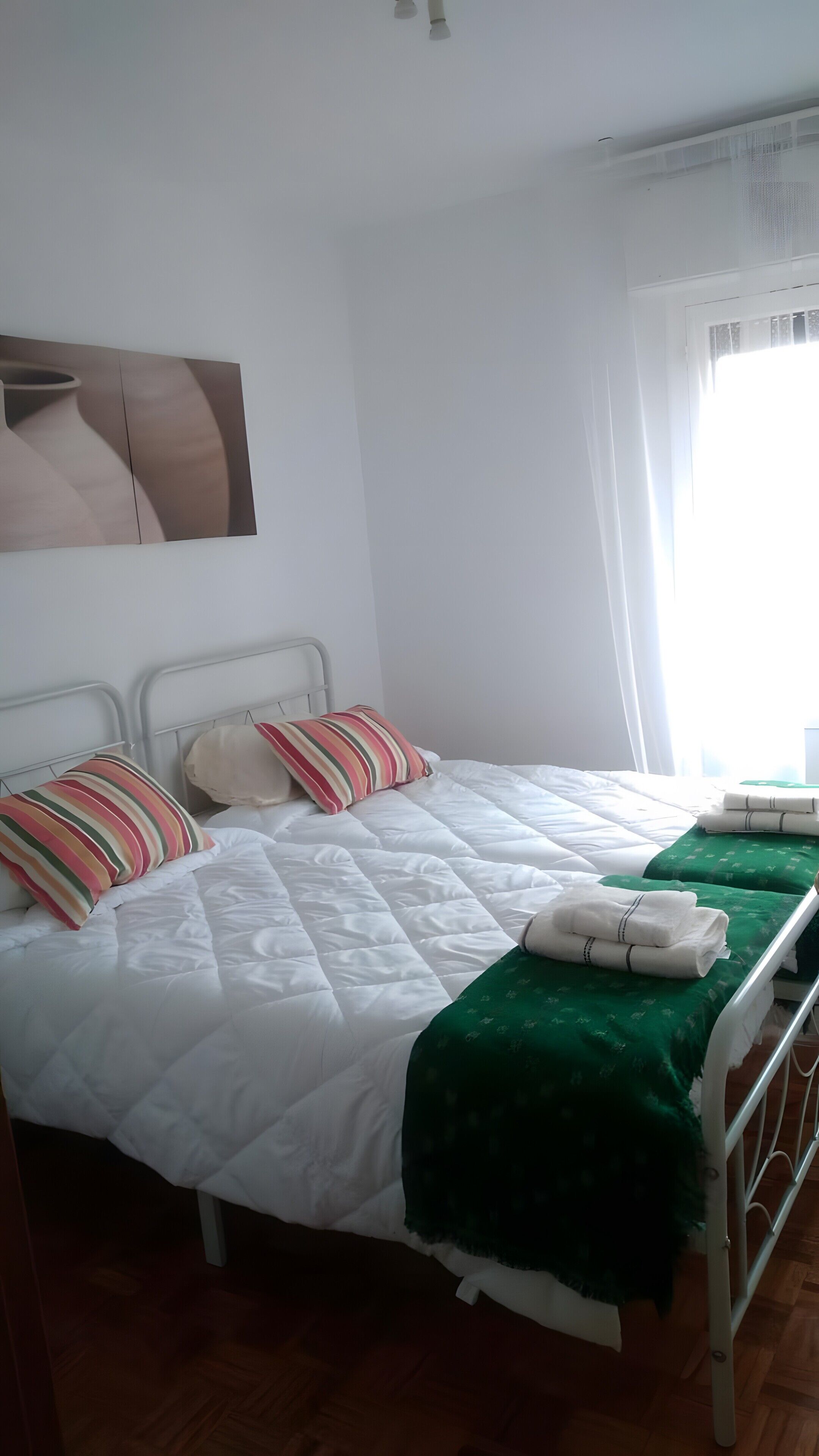 Hotellihuone, jossa on sänky, tyynyjä, vihreä peitto ja ikkuna, jossa on verhot.