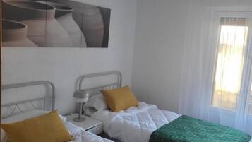 A room with two beds, each with a distinct green and yellow bedspread, a bedside table with a lamp, and a wall-mounted artwork.