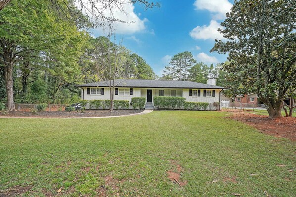 A single-story house with a front porch, surrounded by a well-maintained lawn and trees.