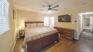Ein Schlafzimmer mit Bett, Deckenventilator, Nachttisch, Kommode und Fernseher.
