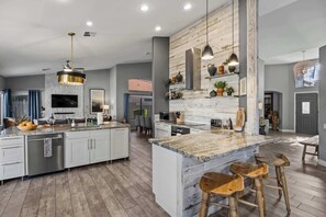 A spacious kitchen with a large island, modern appliances, and a rustic wooden accent wall. - LUX Modern Escape: Pool, Putt, Kierland Commons (Scottsdale)