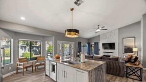 A modern kitchen with a central island, white cabinetry, and a dining area with a wooden table and chairs. - LUX Modern Escape: Pool, Putt, Kierland Commons (Scottsdale)