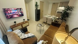 Una sala de estar con un sofá marrón, una mesa redonda pequeña y un televisor montado en la pared.
