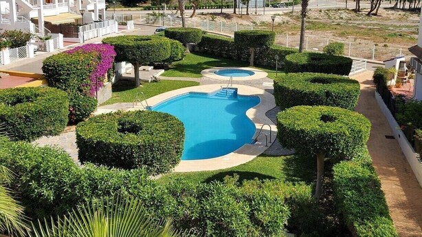 Un resort con piscina rodeada de arbustos cuidados y palmeras.