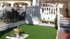 Un edificio blanco con balcones, un pequeño jardín con césped artificial y una fuente.
