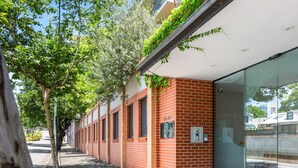 A brick building with a glass entrance, a tree-lined sidewalk, and a clear sky. - Green Views & Great Location: Inner-city 1-bed (Sydney)