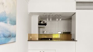 A modern living room with a grey sofa, colorful pillows, and a kitchen area with white cabinets and a gold backsplash. - Green Views & Great Location: Inner-city 1-bed (Sydney)