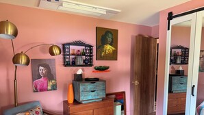 Una stanza con una parete rosa, un comò in legno, una poltrona blu, una lampada da terra e un tappeto colorato.