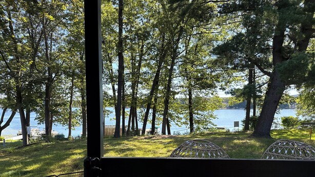 Vista da un balcone su un lago, con alberi e una zona erbosa.