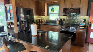 Una cucina moderna con mobili in legno, un piano di lavoro in granito, un frigorifero in acciaio inossidabile, un fornello e una finestra vista verde.