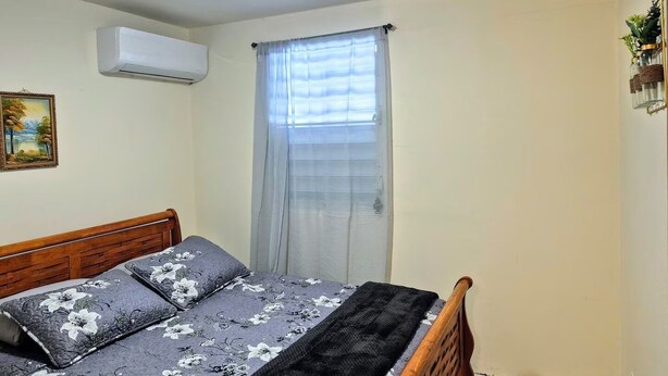 Ein Schlafzimmer mit Bett, einem Vorhangfenster, einer Klimaanlage und einem gerahmten Bild an der Wand.