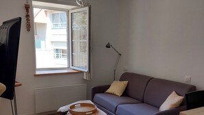 A modern living room with a grey sofa, a wooden coffee table, a standing lamp, and a window with a view of buildings. - Ty PenAr Pont étage (Saint-Pol-de-Léon)