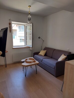 Un salon moderne avec un canapé gris, une table basse en bois, un lampadaire et une fenêtre donnant sur des immeubles.