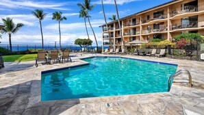 A swimming pool with lounge chairs and a view of the ocean. - Great Location AC & Wifi Concierge Included! (Kailua-Kona)