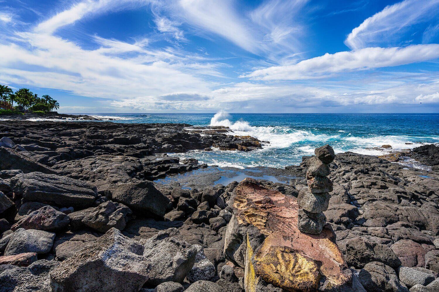 A rocky coastline with waves crashing against the shore, under a clear blue sky.