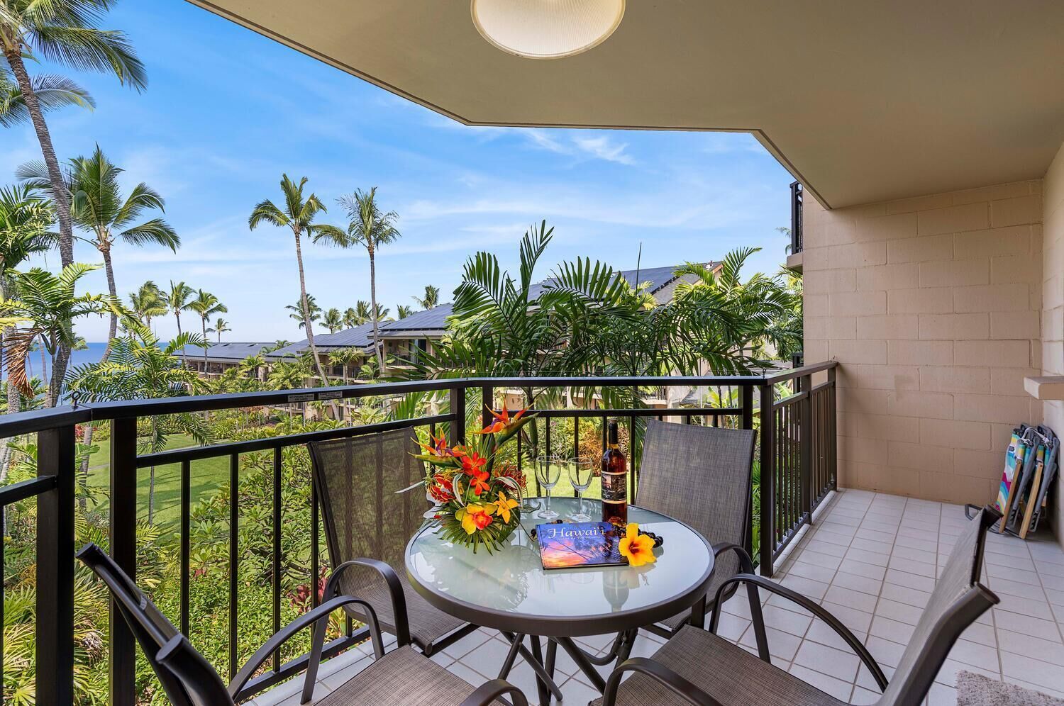 A balcony with a round glass table, two chairs, a flower arrangement, and a bottle.