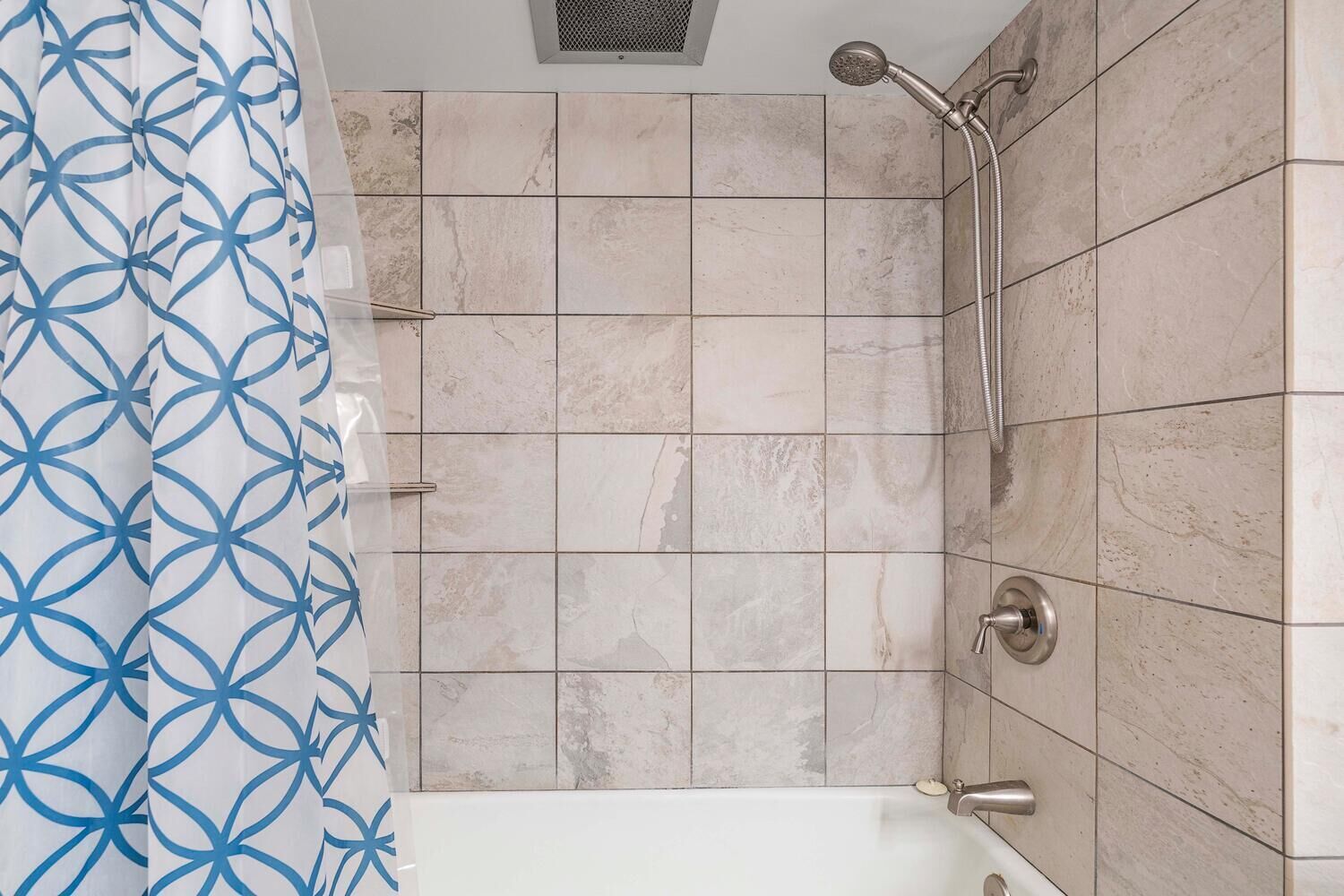 A bathroom with a shower, a bathtub, and a curtain with a geometric pattern.