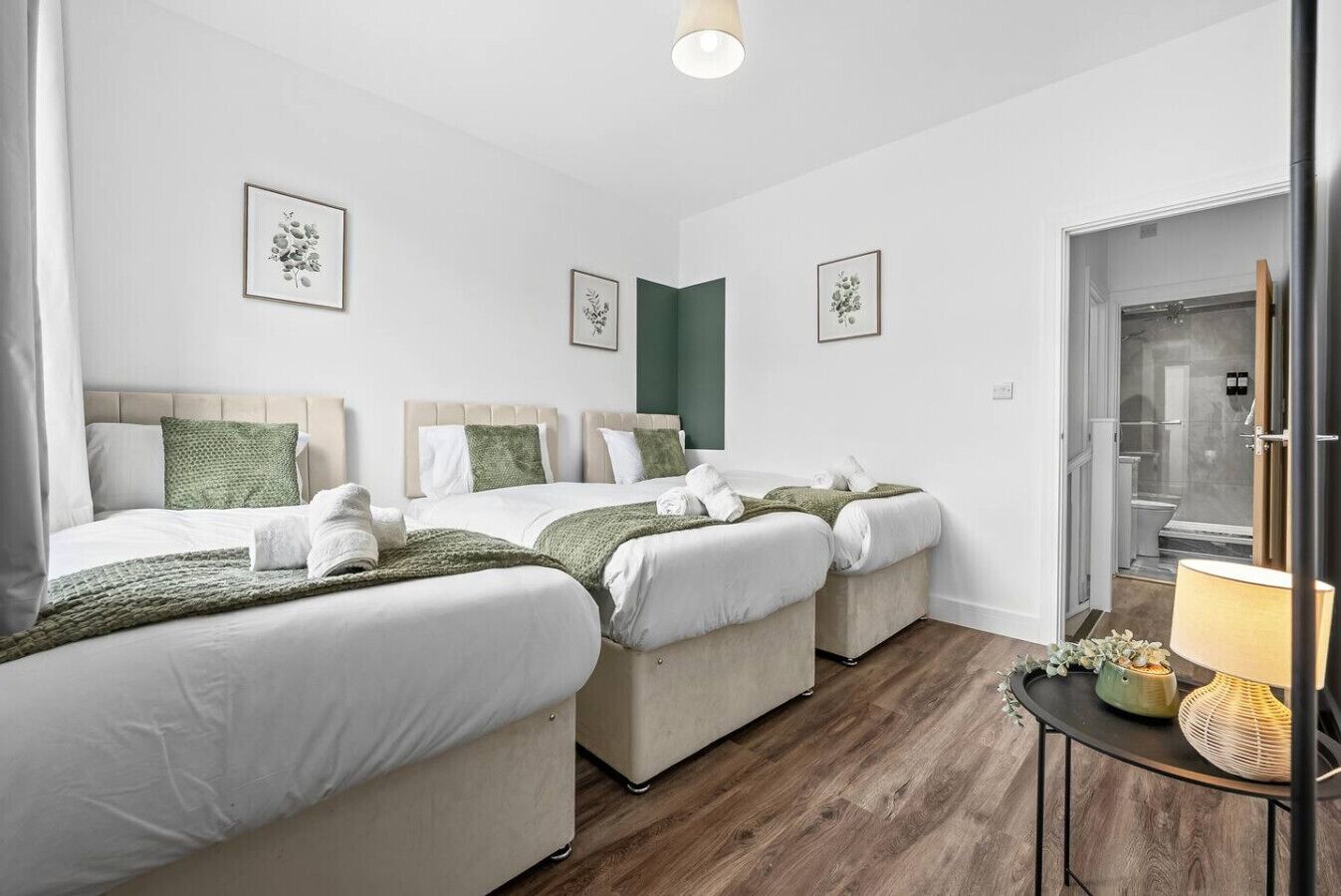 Ein Hotelzimmer mit drei Betten, Holzboden und einem durchgegangenen Tür erkennbaren Badezimmer.