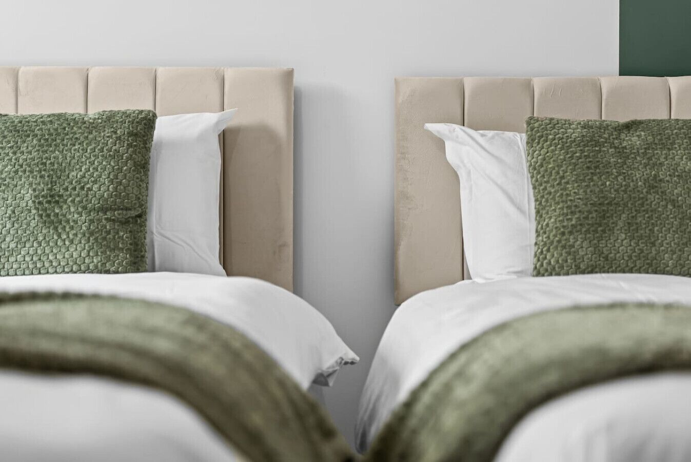 Ein Doppelbett mit beigezogener Kopfstütze, weißen und grünen Kissen sowie einer grünen Decke.