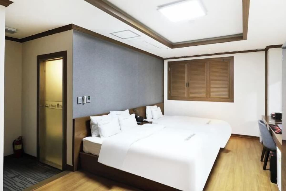 A hotel room with a large bed, a desk, a chair, a wardrobe, and a door.