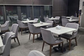 A modern dining area with tables and chairs, large windows, and a view of the city. - Bolton Hotel (Gwangju)