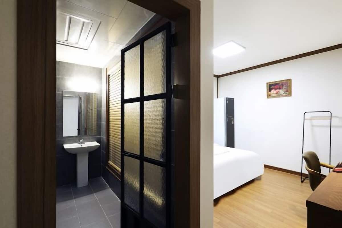 A room with a bed, a desk, a chair, a small sink, and a frosted glass door.