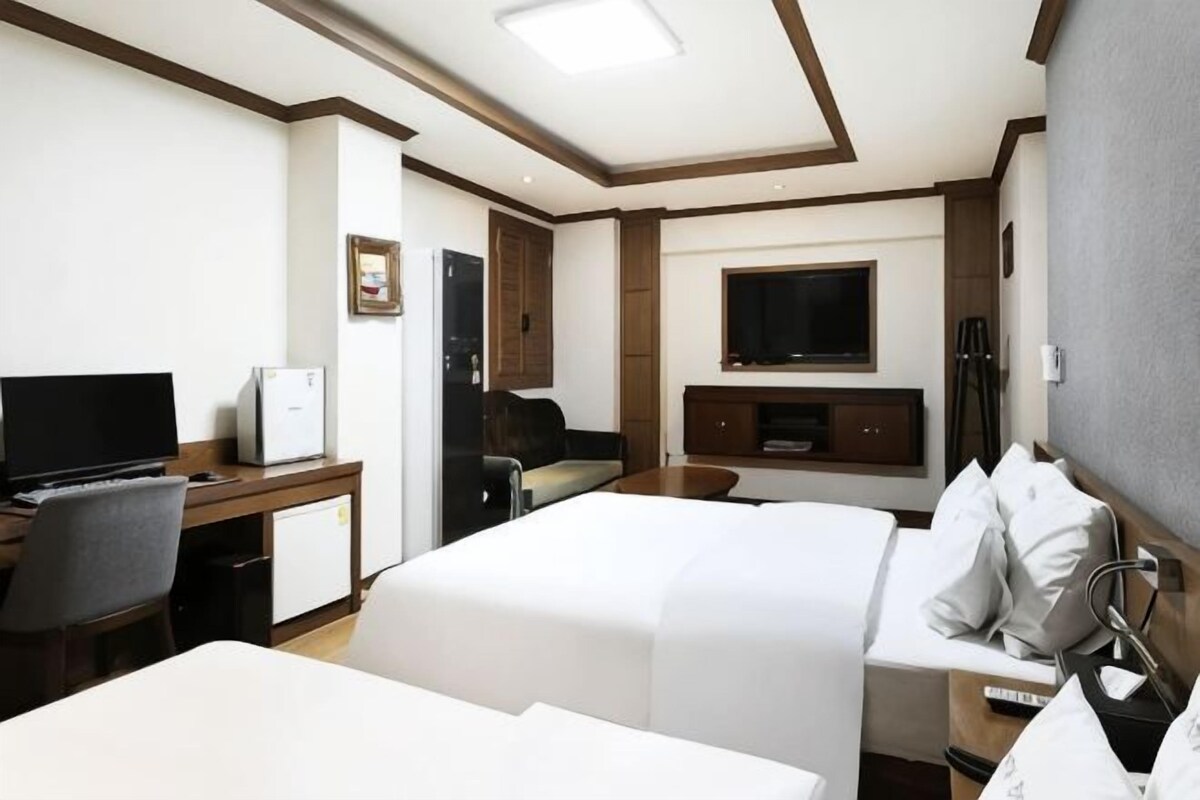 A hotel room with two beds, a desk with a computer, a television, and a minibar.