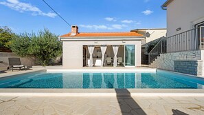 Ein modernes Poolhaus mit einem gepflasterten Dach, einer Glastür, die auf eine Terrasse führt, und einem Kiespool.