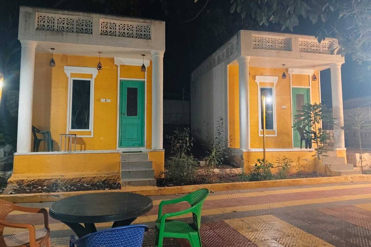 Two yellow buildings with green doors and windows, each with a small porch and steps leading up to the entrance.