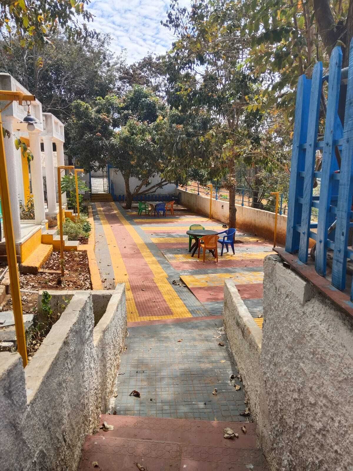A staircase leading to a covered outdoor area with a table and chairs, surrounded by trees and a blue gate.