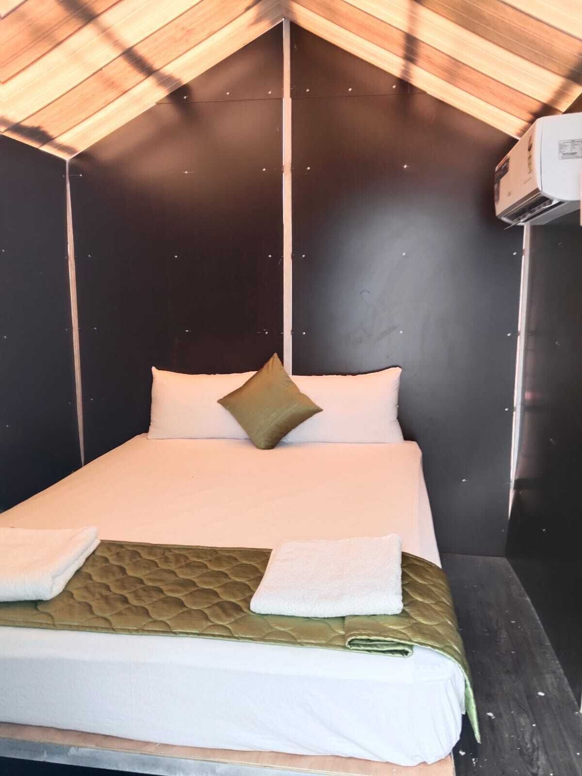 Een enkel bed met een gewatteerd hoofdeinde, twee kussens en een opgevouwen handdoek ernaast.
