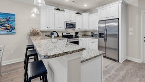 A modern kitchen with white cabinets, a granite countertop, stainless steel appliances, and pendant lighting. - Yellow Fin Retreat (Murrells Inlet)