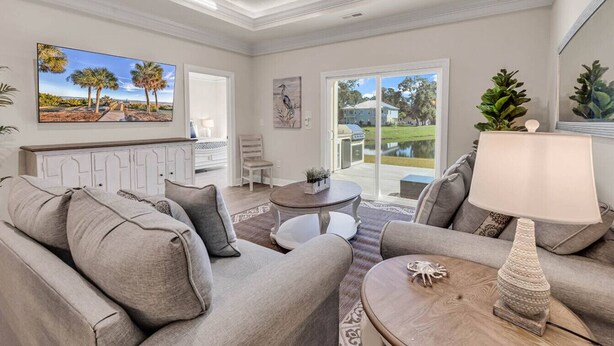 A spacious living room with a grey sofa set, a coffee table, and a lamp. There is a painting on the wall and a view of the outdoors through the glass door. - Yellow Fin Retreat (Murrells Inlet)