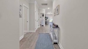 A hallway with a wooden floor, a blue rug, white walls, and a small table with decorative items. - Yellow Fin Retreat (Murrells Inlet)