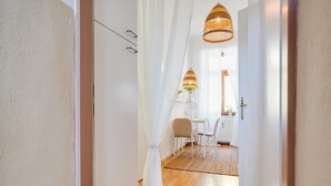 A hallway with a white door, a dining area with a table and chairs, and a hanging wicker lamp. - Arcadio Home - Smart Suite (Graz)