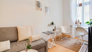 A modern living room with a grey sofa, white chairs, a small table with a vase, and a window with sheer curtains. - Arcadio Home - Smart Suite (Graz)