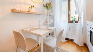 A dining area with a white table, two chairs, a hanging light fixture, and a window with sheer curtains. - Arcadio Home - Smart Suite (Graz)