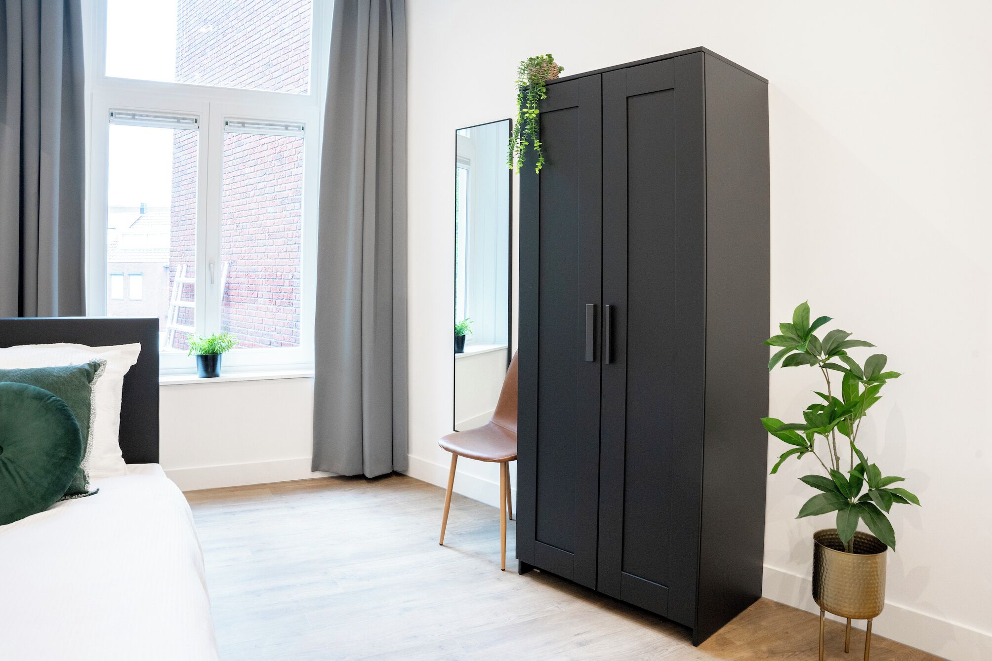 Une chambre à coucher avec un lit, une armoire sombre, une chaise et une plante en pot.
