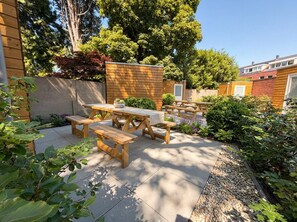 An outdoor patio with wooden tables and benches, surrounded by a garden with various plants and trees. - Discover your ideal Tilburg stay at Bed en Koffie Hanno – a newly built 1-bedroom apartment designed for comfort and ease. Enjoy all-inclusive utilities, regularly cleaned shared spaces, and a peaceful garden to unwind in. (Tilburg)